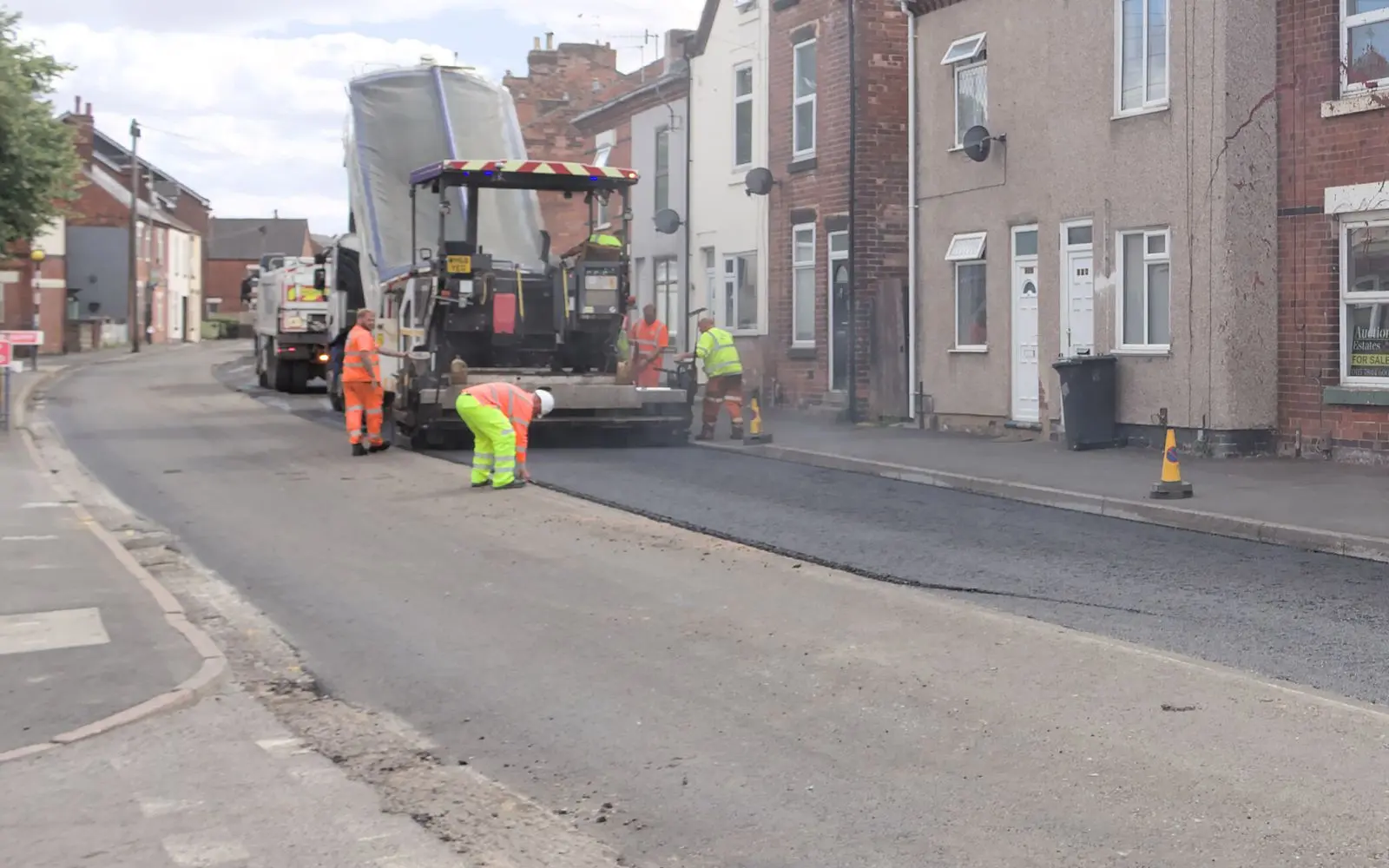 A surfacing crew in high-visibility clothing laying new asphalt on a terraced street